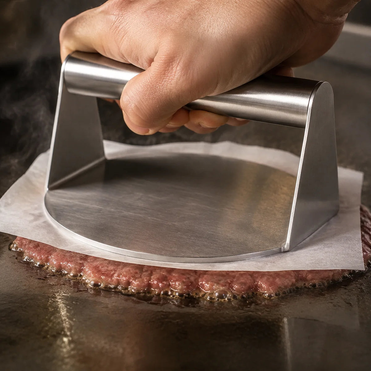 Close-up of WAFORA SmashPress flattening beef beneath parchment on a hot griddle