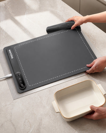 WAFORA™ TableWarm XL roll-up food warming mat displayed on a countertop with hands preparing a dish.