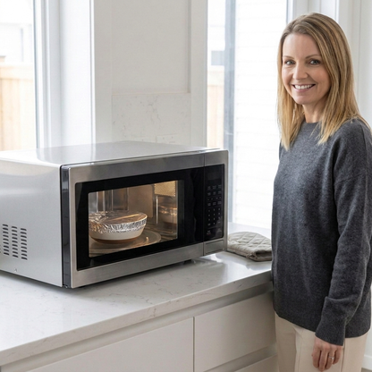A woman standing beside a microwave in a bright kitchen, with food heating inside the WAFORA FreshCap dietary supplement.